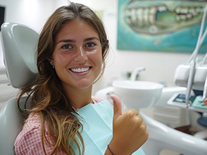 Happy young woman in dental chair making thumbs-up gesture