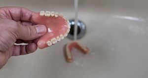 Person rinsing dentures in a sink