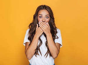 Young woman with wide eyes covering her mouth